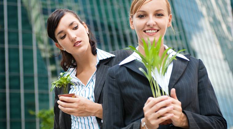 Two competitive businesswomen cupping their plants in their hands