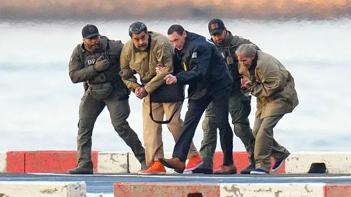 Venezuelan President Nicolas Maduro and First Lady Cilia Flores appear in handcuffs following their arrival at a Manhattan helipad on January 5, 2026. The couple is shown being escorted by armed federal officers toward an armored vehicle for transport to a federal courthouse in Manhattan. (TheImageDirect.com) 