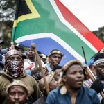 Members of South Africa's traditional Zulu warrior corps, the Amabutho, carried the national flag as they marched in Durban on June 30, 2026, joining a demonstration organized by the "March and March" movement. The protest coincided with a deadline that citizen-led groups had unilaterally set for undocumented foreign nationals to leave the country/AP