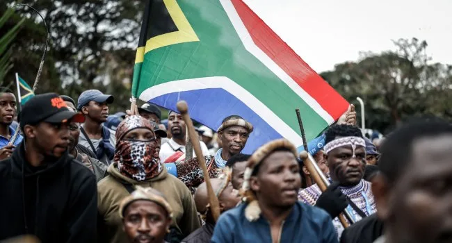 Members of South Africa's traditional Zulu warrior corps, the Amabutho, carried the national flag as they marched in Durban on June 30, 2026, joining a demonstration organized by the "March and March" movement. The protest coincided with a deadline that citizen-led groups had unilaterally set for undocumented foreign nationals to leave the country/AP